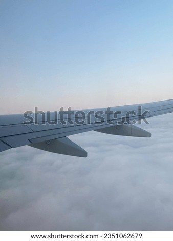 Airplane wing on top of a layer of clouds. The sky is light blue and has a dash of pink. Soft and calm atmosphere. Holiday pictures. Going to a vacation, European holiday, global tourists