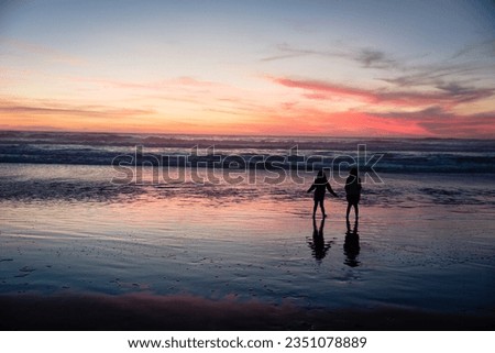 Silhouettes of two girls or young women playing at a beach at sunset