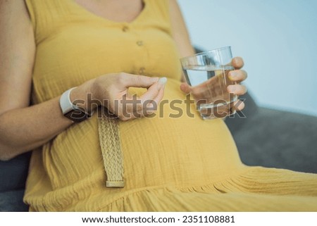 Prenatal Vitamins. Portrait Of Beautiful Smiling Pregnant Woman Holding Supplement and a glass of water, Taking Supplements For Healthy Pregnancy While Sitting On Couch At Home, Free Space Royalty-Free Stock Photo #2351108881