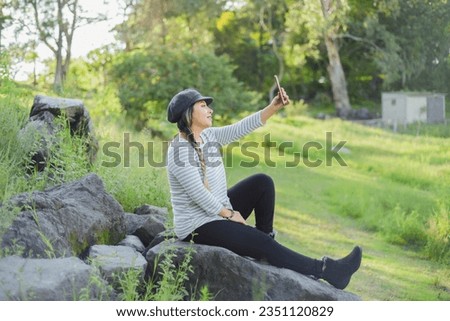 Woman taking a selfie seated on a rock in the middle of nature.