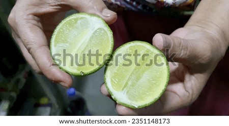 a photography of a person holding two limes in their hands, lemons are cut in half and held in a person's hands.