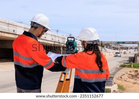 Two engineer use theodolite equipment and looking blueprints construction project for route surveying to build a bridge across the intersection to reduce traffic congestion during rush hours.
