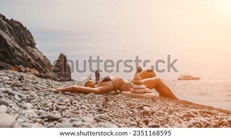 Woman bilds stones pyramid on seashore on a sunny day on the blue sea background. Happy holidays. Pebble beach, calm sea, travel destination. Concept of happy vacation on the sea, meditation, spa.