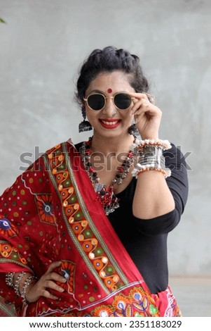 Indian woman in a stylish traditional look for Navratri for playing Garba and dandiya wirh sun glasses and fabric and oxidized jewelry. red and black outfit with traitional bangles earings, bindi. Royalty-Free Stock Photo #2351183029