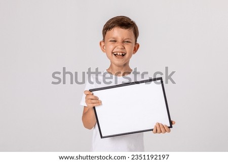 portrait of happy laughing baby boy holding white drawing Board on white background, young boy is holding a drawing board in her hands. white isolated background. Mock up. Copyspace. Royalty-Free Stock Photo #2351192197