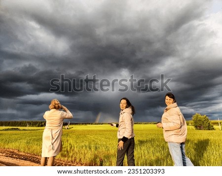 Tourist girls take pictures of a rainbow and dramatic, gloomy clouds over a field on a spring, summer, autumn day. The concept of the beauty of nature and travel