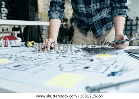 Interior designer or architect reviewing blueprints and holding pencil drawing on desk at home office.