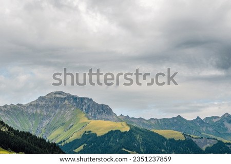 Panoramic view of mountain ridges and slopes with green pastures in summer and cloudy sky in the background. A view to Gsür 2708 m., a mountain in the Bernese Alps, Adelboden, Switzerland.
 Royalty-Free Stock Photo #2351237859