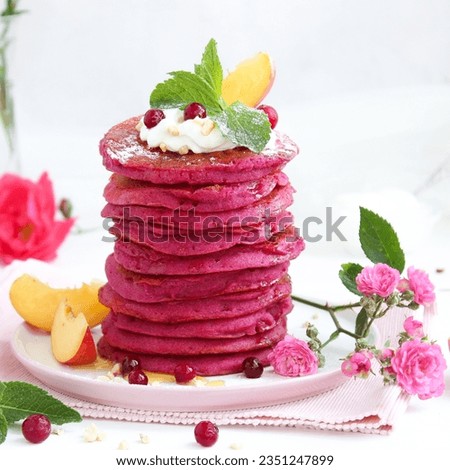 Atmospheric, stylized photo of a stack of natural pink pancakes adorned with cream, fresh peaches, and currants, complemented by a vase with live flowers on the side