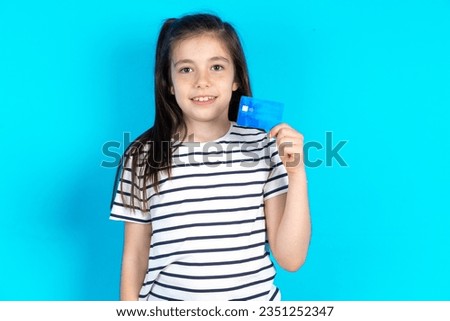 Photo of happy cheerful smiling positive Beautiful caucasian kid girl standing over blue studio background recommend credit card