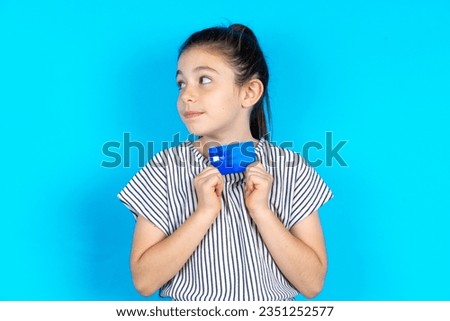 Photo of cheerful Beautiful caucasian kid girl standing over blue studio background hold debit card look empty space