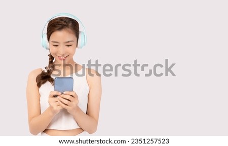 Beautiful Young Asian Woman wearing wireless headphones and listening to music and using phone Young Asian teen lady using smart phone for listening music in headphones isolated on white background