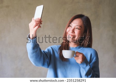 Portrait image of a beautiful young asian woman using mobile phone to take a selfie while drinking coffee
