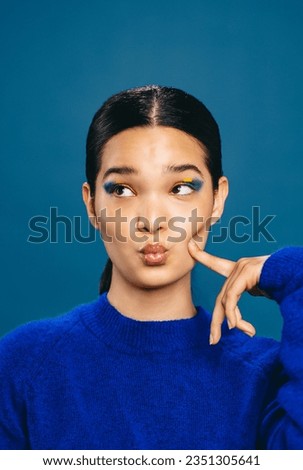 Woman showcasing a trendy makeup look, she pouts her lips and makes a face while wearing a bold straight line eyeliner. Playful young woman radiating confidence and attractiveness. Royalty-Free Stock Photo #2351305641