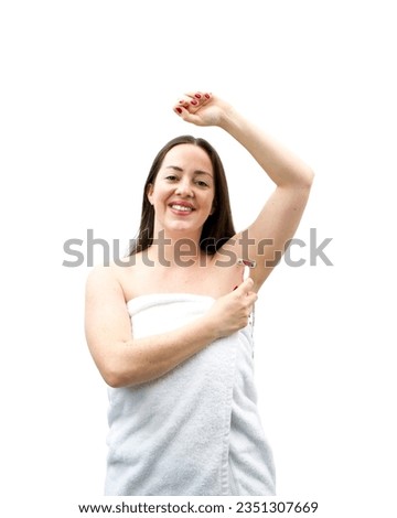 Pretty young brunette woman wearing a towel while shaving her arm pit with a razor against a white background