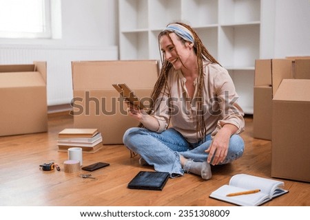 Modern ginger woman with braids looking at photo in frame while moving into new home.