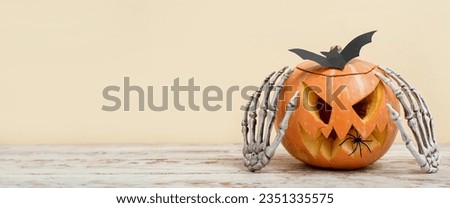 Skeleton hands, pumpkin and paper bat on table against beige background with space for text. Halloween banner