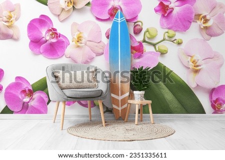 Wooden surfboard with armchair and houseplant near wall with printed orchid flowers