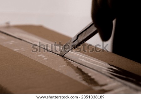 Close-up of woman's hand opening box using cutter. Hands unpacking cardboard boxes in the house. Royalty-Free Stock Photo #2351338189