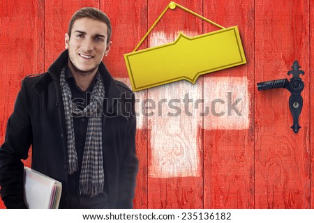 Smiling student in front of wooden door with golden plate in swiss flag colors