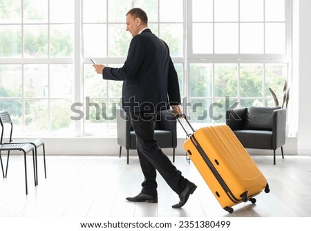 Mature businessman with passport and suitcase walking in hall of airport