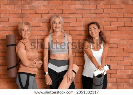 Sporty mature women with yoga mats near brick wall