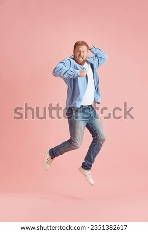 Full-length image of bearded mature man in casual clothes emotionally jumping and shouting over pink studio background. Concept of human emotions, lifestyle, facial expression, ad. Copy space for ad