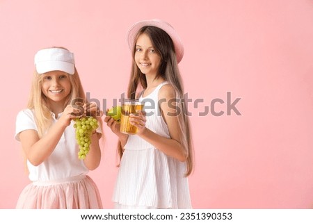 Little girls with glass of juice, grapes and apple on pink background