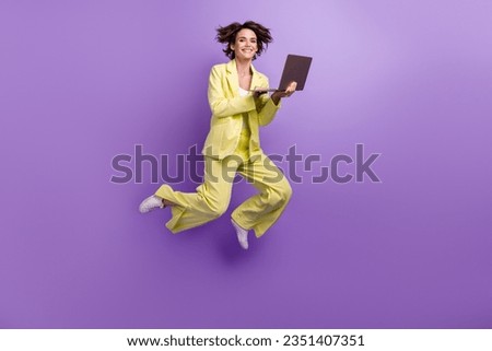 Full length photo of cute shiny woman dressed yellow jacket working modern device jumping high isolated purple color background