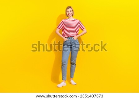 Full length photo of pretty adorable woman dressed striped t-shirt jeans standing arms in pockets isolated on vibrant yellow background