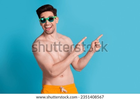 Photo portrait of nice young male finger point empty space wear trendy yellow shorts isolated on blue color background summer vacation