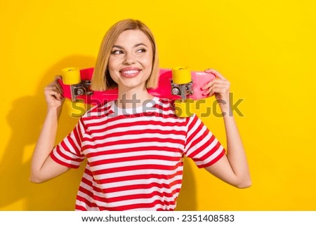 Photo of cute woman dressed striped t-shirt hold skateboard behind head look at offer empty space isolated on vibrant yellow background