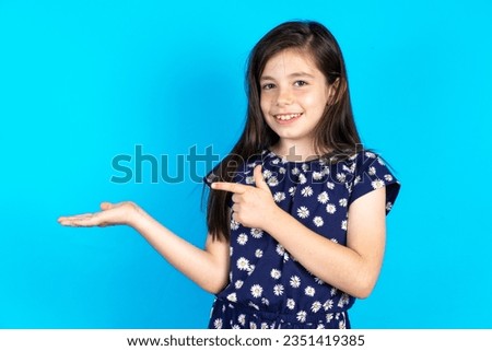 Positive caucasian kid girl wearing floral dress promoter point index finger copyspace hold hand demonstrate offer ads promo