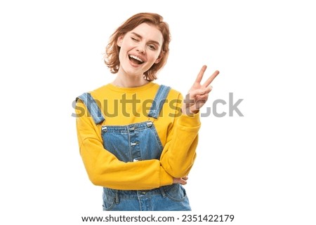 Portrait of young happy redhead woman in yellow casual showing peace and love gesture with fingers isolated on white studio background