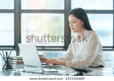 Charming young businesswoman sitting in bright office and working with modern devices.	