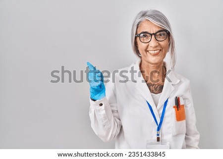 Middle age woman with grey hair wearing scientist robe doing happy thumbs up gesture with hand. approving expression looking at the camera showing success. 