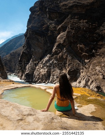 Young Woman Sits next to the Santo Tomas Hot Springs with a Beautiful Landscape of Mountains and Turquoise River in Abancay, Peru 