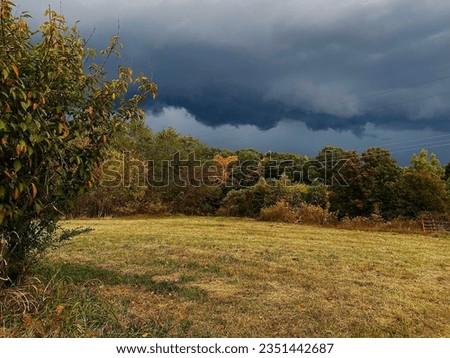 Dark blue and gray storm clouds are seen moving in from the left side of the picture. There is an autumn scenery underneath the storm clouds.