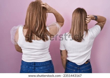 Hispanic mother and daughter wearing casual white t shirt over pink background backwards thinking about doubt with hand on head 