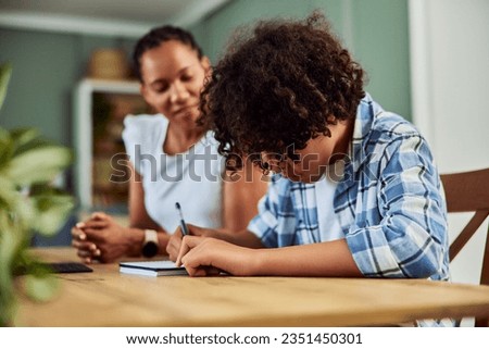 African American teen boy doing homework, making notes in the notebook at the table, side view. Royalty-Free Stock Photo #2351450301
