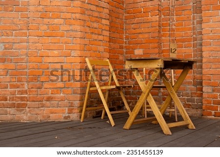 Wooden terrace with a table and a chair against the background of a brick building with a sign with a table number for reservation table in a summer cafe