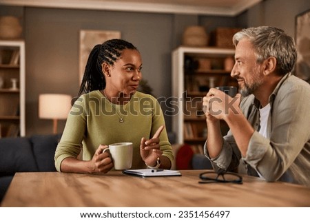 Two experienced individuals are deep in conversation while enjoying a comforting drink at their home table. Royalty-Free Stock Photo #2351456497