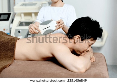 Therapist and male patient performing hair removal treatment on the back
