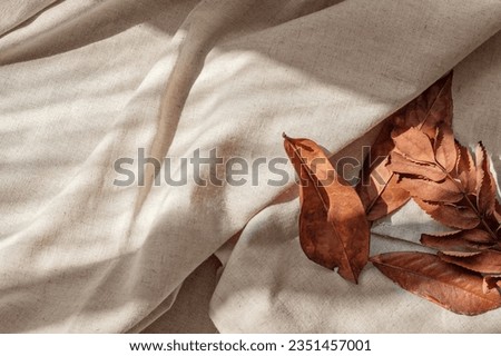 Messy brown fall leaves on neutral beige linen crumpled fabric background with aesthetic natural sunlight shadows. Lifestyle boho business brand template. Royalty-Free Stock Photo #2351457001