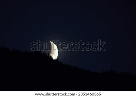 the moon setting over the mountain with tree silhouettes in the foreground