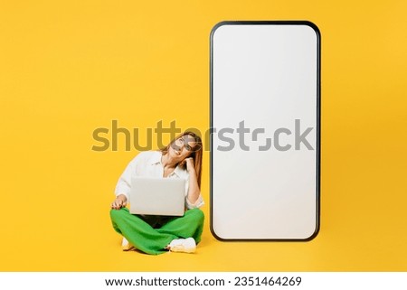 Full body young happy IT woman she wears white shirt casual clothes big huge blank screen mobile cell phone hold use work on laptop pc computer smartphone with area isolated on plain yellow background