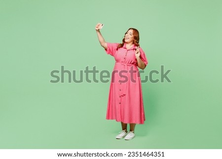 Full body young chubby redhead woman wear casual clothes pink dress doing selfie shot on mobile cell phone post photo on social network show victory gesture isolated on plain green color background