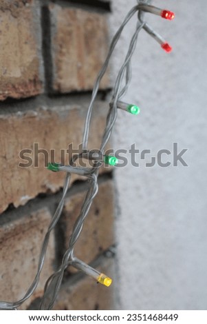 Up close picture of string LED lights yellow, green and red, brick wall in background