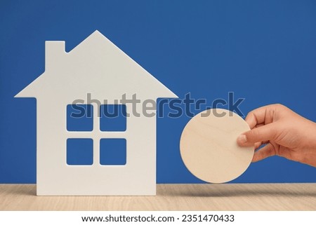 Real estate rental banner. White model of a house and a hand holding a sign mockup for an inscription as a symbol of rental housing. High quality photo.