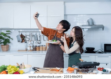 Happy of loving young asian Take a selfie with a smartphone of having fun standing a cheerful preparing beef steak food and enjoy cook cooking with vegetables standing on a kitchen Condo life or home